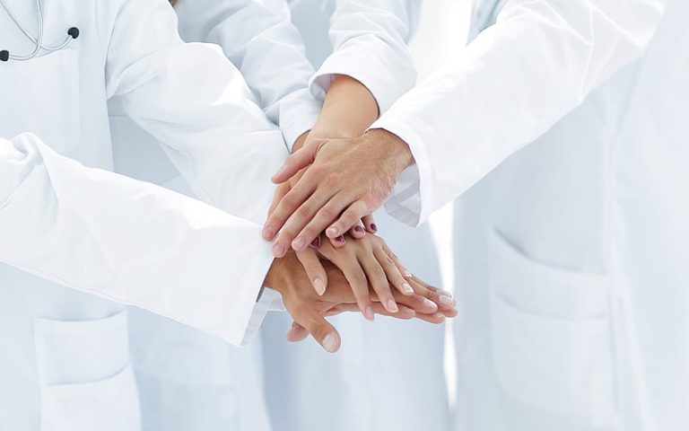 Brazos de médicos y sus manos juntas diciendo "todos a una)